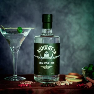 A bottle of Runway 28 Irish Craft Gin beside a martini glass and botanicals